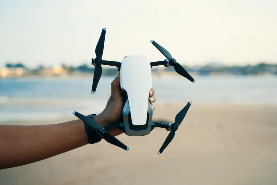 Mano sosteniendo un dron plegable frente al mar