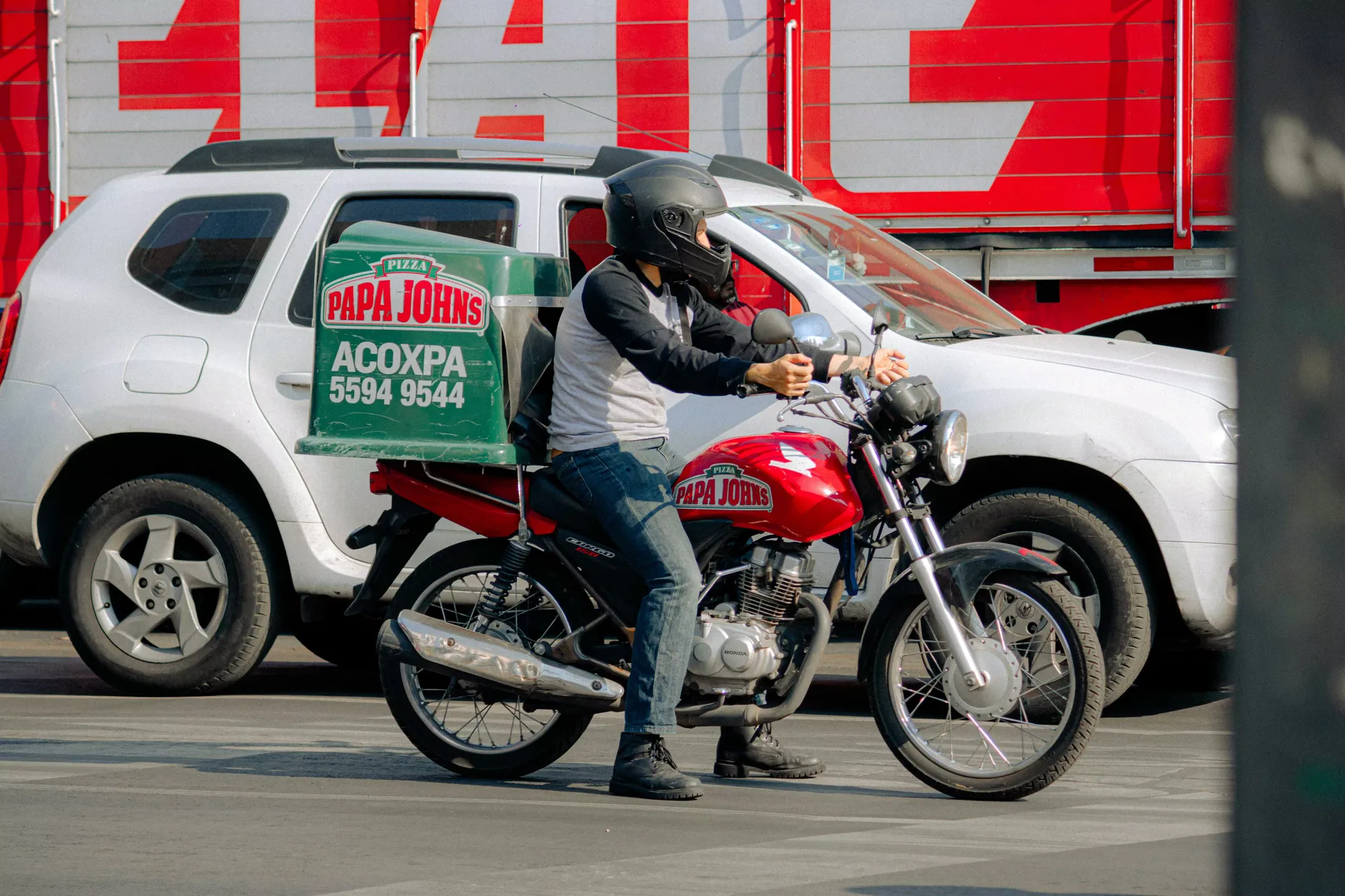 Motociclista de reparto junto a un carro en la calle