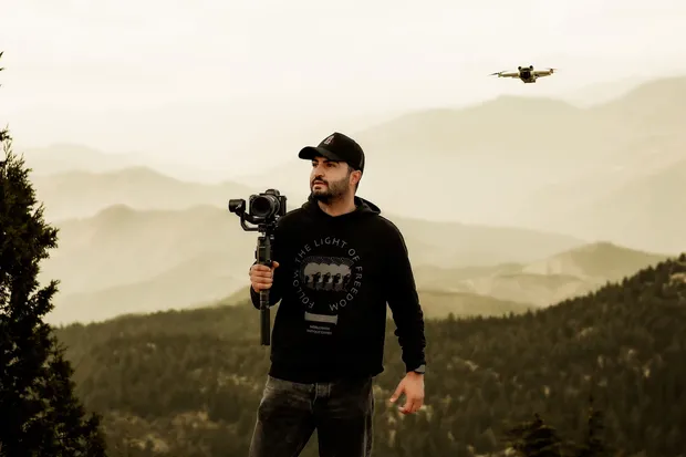 Camarógrafo con estabilizador y un dron volando sobre las montañas