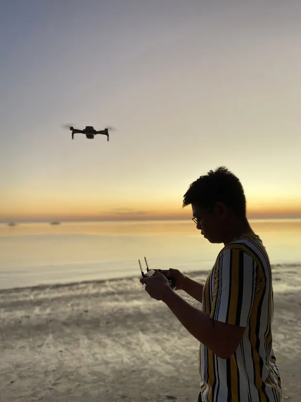 Persona pilotando un dron en la playa al atardecer