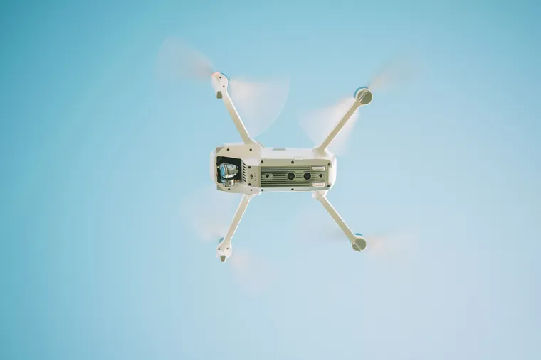 Dron blanco visto desde abajo, volando contra un cielo azul