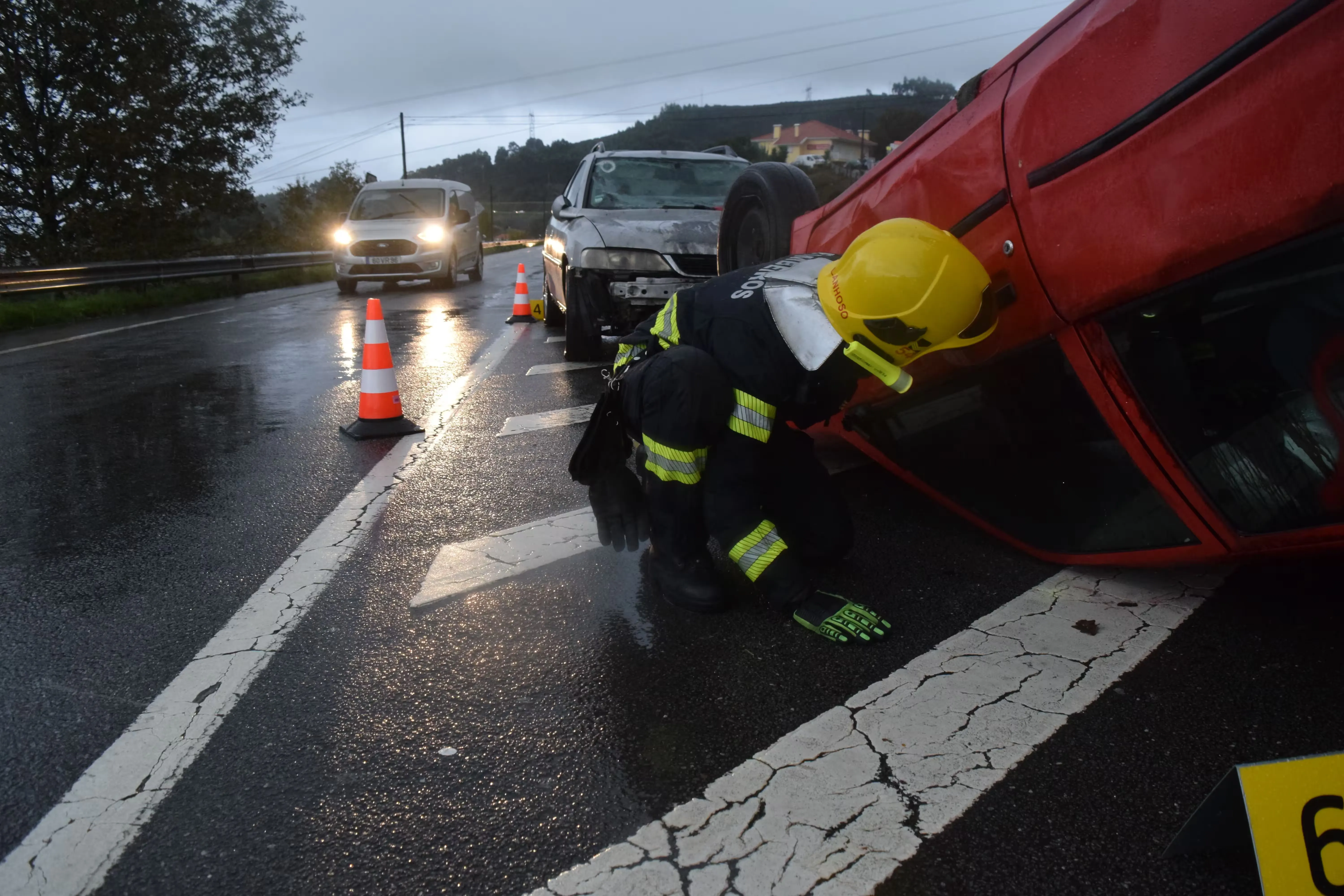 Un bombero atiende un carro accidentado en una vía mojada