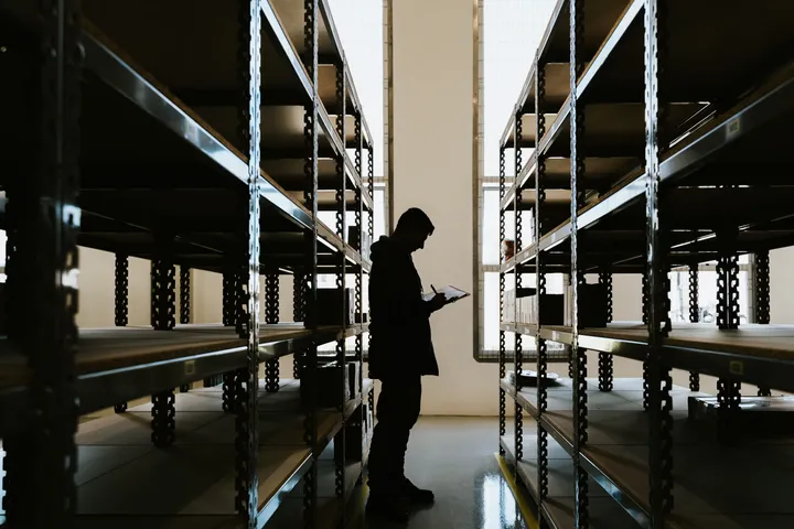 Persona revisando inventario entre estanterías de una bodega